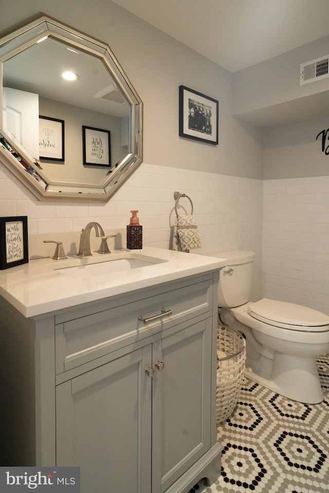 bathroom with visible vents, vanity, toilet, tile walls, and a wainscoted wall