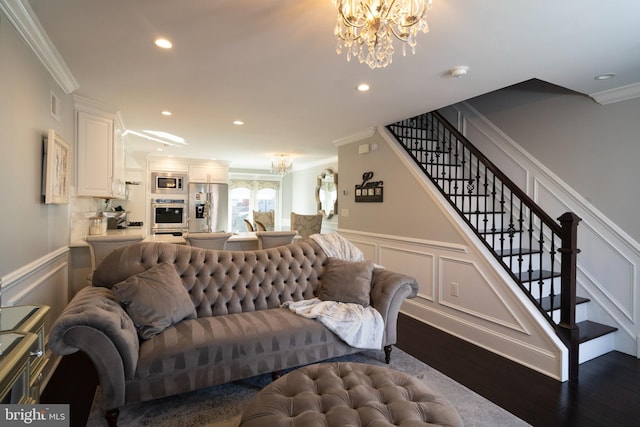 living room with ornamental molding, a decorative wall, stairway, dark wood-type flooring, and a chandelier