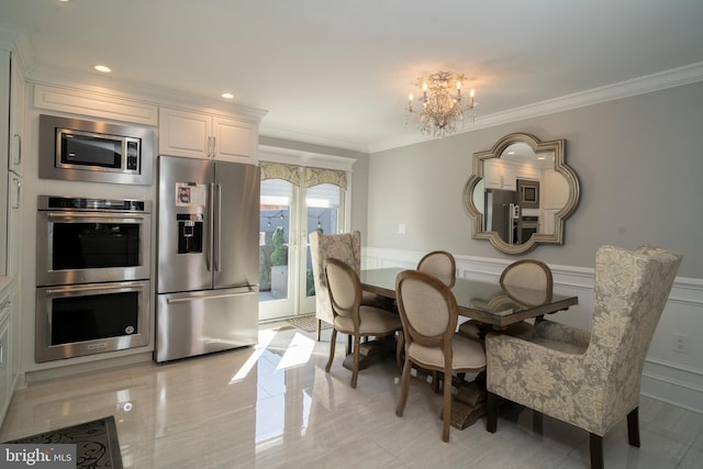 dining space featuring ornamental molding, wainscoting, a decorative wall, and a chandelier