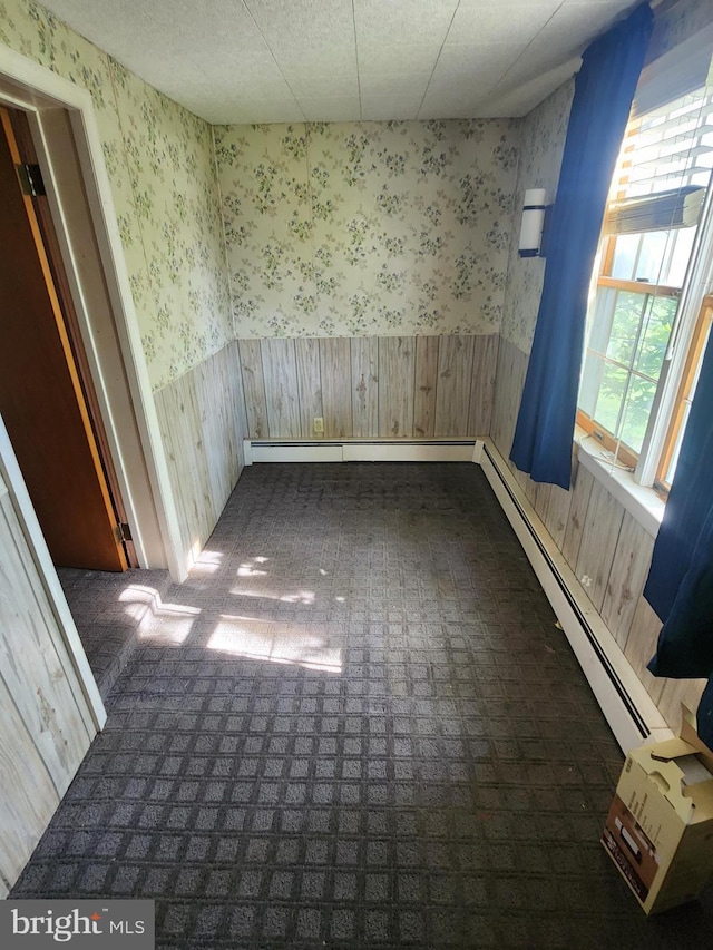 unfurnished room with wooden walls, baseboard heating, wainscoting, and wallpapered walls