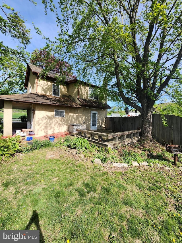 back of house featuring a lawn, fence, and stucco siding
