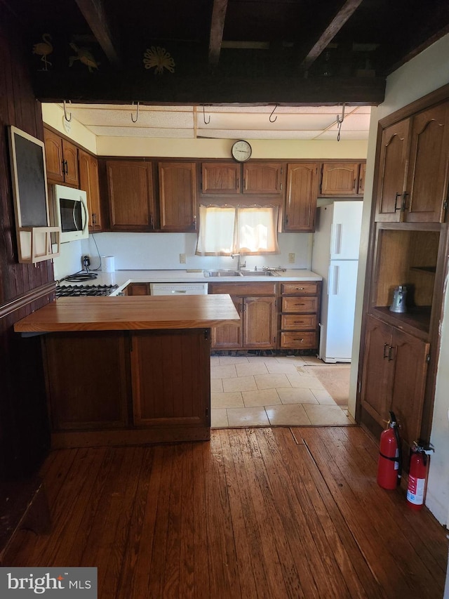 kitchen with brown cabinets, a sink, white appliances, hardwood / wood-style floors, and a peninsula