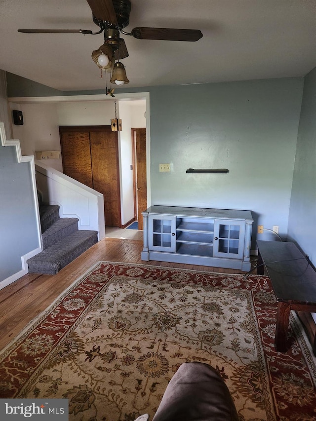 living room with a ceiling fan, wood finished floors, and stairway