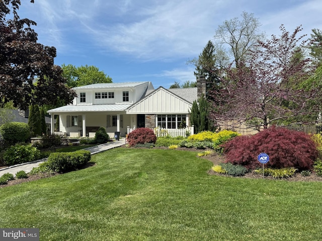 view of front facade featuring a front lawn, stone siding, a chimney, board and batten siding, and a porch