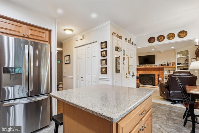 kitchen with crown molding, light stone counters, a brick fireplace, a kitchen island, and stainless steel refrigerator with ice dispenser