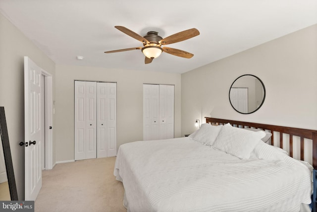 bedroom featuring light colored carpet, a ceiling fan, multiple closets, and baseboards
