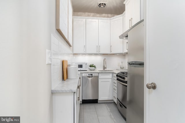 kitchen with light tile patterned flooring, appliances with stainless steel finishes, a sink, white cabinetry, and tasteful backsplash