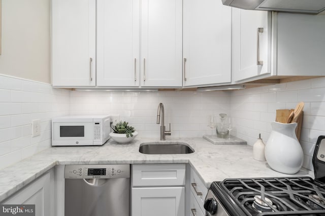 kitchen featuring white microwave, gas range oven, white cabinets, a sink, and dishwasher