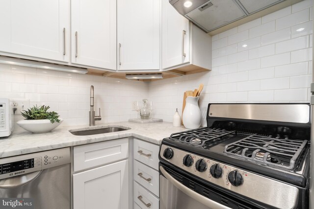 kitchen with a sink, stainless steel appliances, white cabinetry, custom range hood, and backsplash