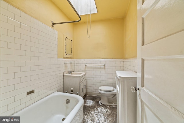 bathroom with vanity, wainscoting, toilet, tile walls, and a tub to relax in