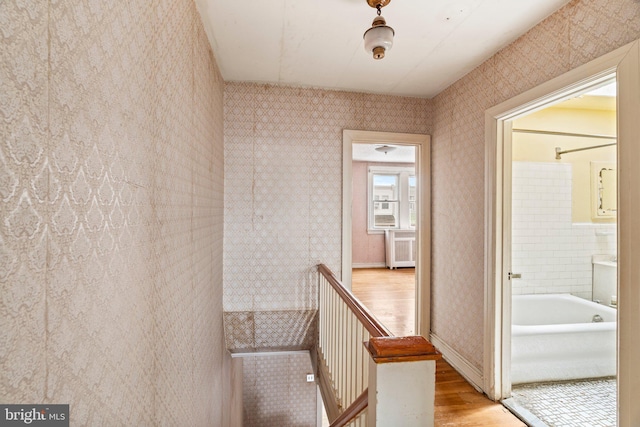 hall featuring baseboards, wallpapered walls, wood finished floors, and an upstairs landing