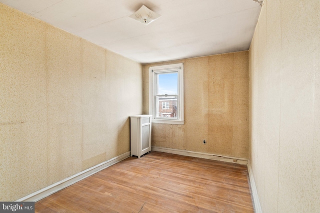 unfurnished room with baseboards, radiator, and wood finished floors