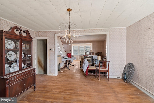 dining area featuring crown molding, wallpapered walls, an inviting chandelier, and wood finished floors