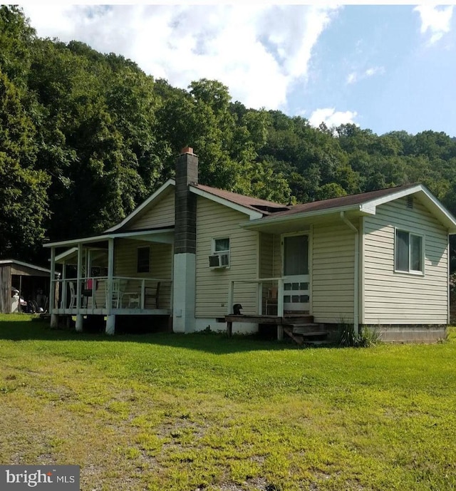 back of property with a porch, a forest view, a yard, and a chimney