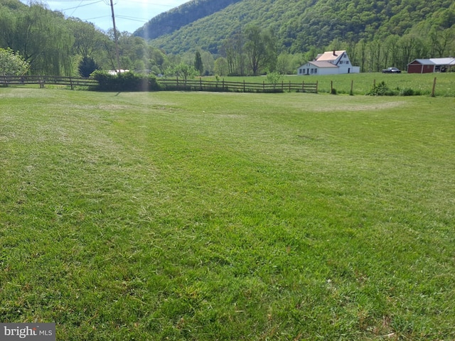 view of yard featuring fence, a view of trees, and a rural view