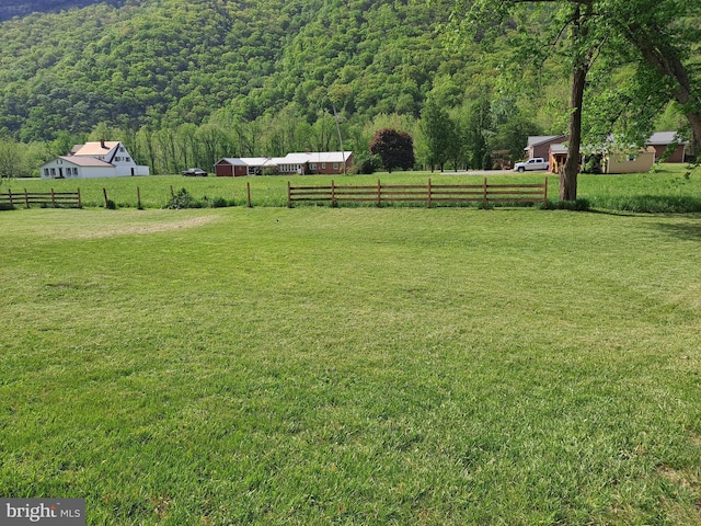 view of yard with a view of trees, fence, and a rural view