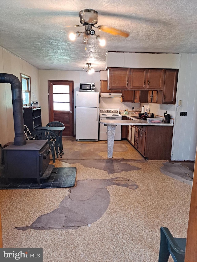 kitchen with a wood stove, electric stove, freestanding refrigerator, stainless steel microwave, and under cabinet range hood