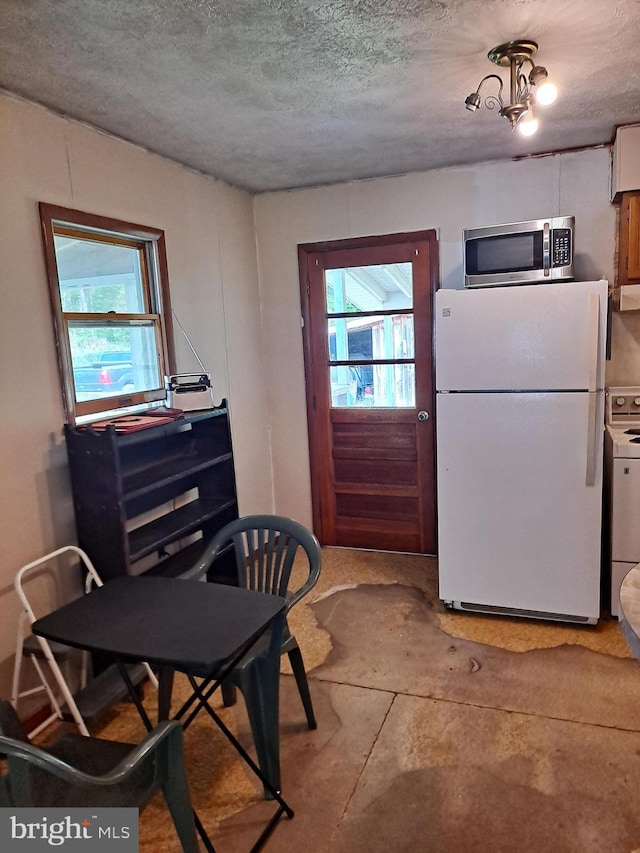 kitchen featuring freestanding refrigerator, a textured ceiling, stainless steel microwave, and washer / dryer