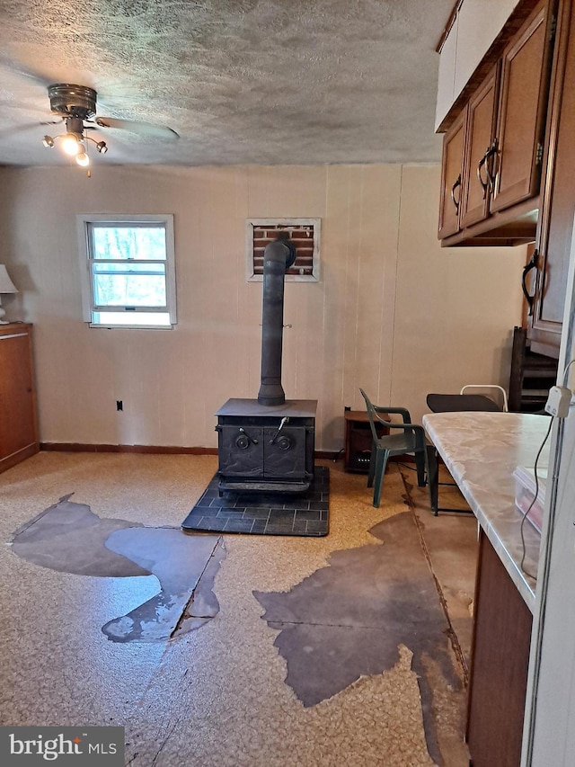 living area featuring baseboards, a ceiling fan, a wood stove, and a textured ceiling