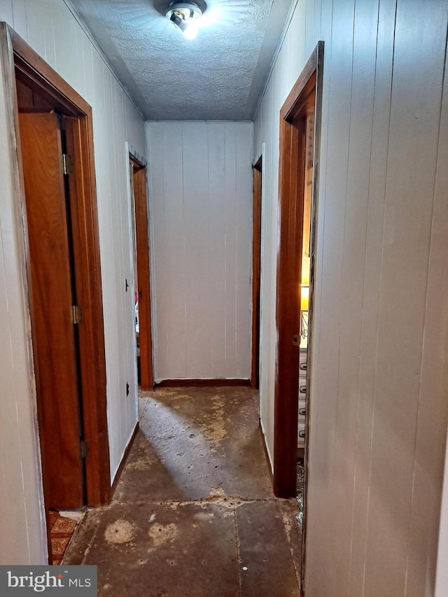 corridor with wood walls, a textured ceiling, and concrete flooring