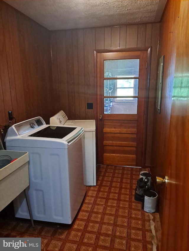 clothes washing area featuring laundry area, washing machine and dryer, wooden walls, a textured ceiling, and tile patterned floors