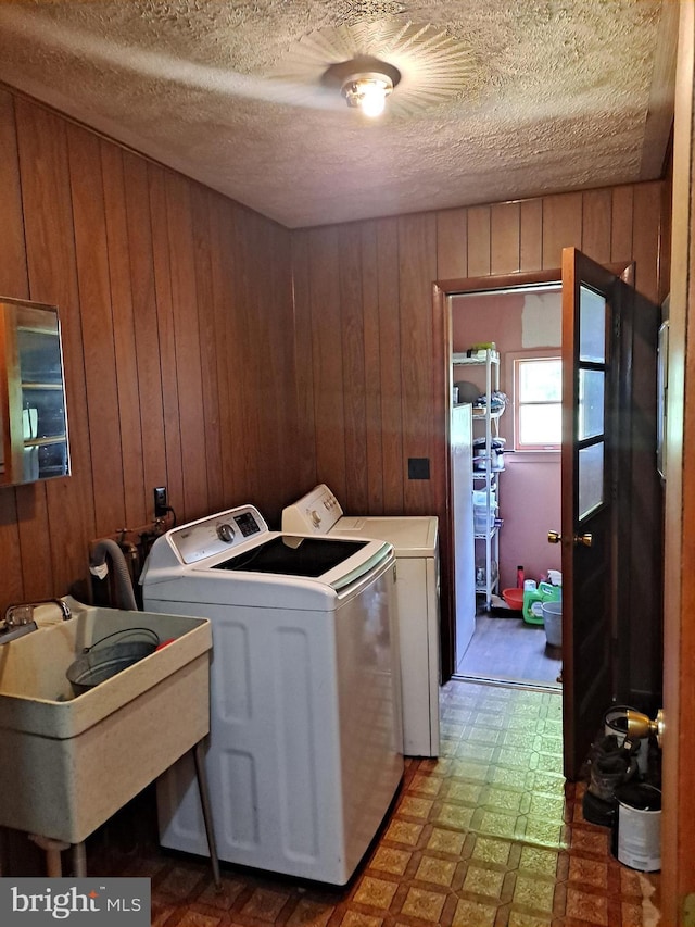 clothes washing area featuring laundry area, wood walls, washer and clothes dryer, tile patterned floors, and a sink