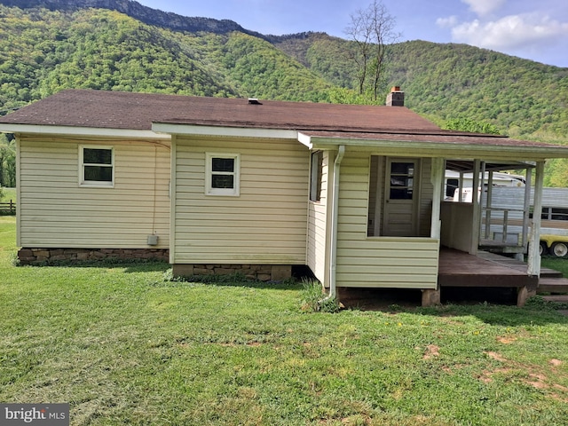 back of property with a lawn, a mountain view, and a chimney