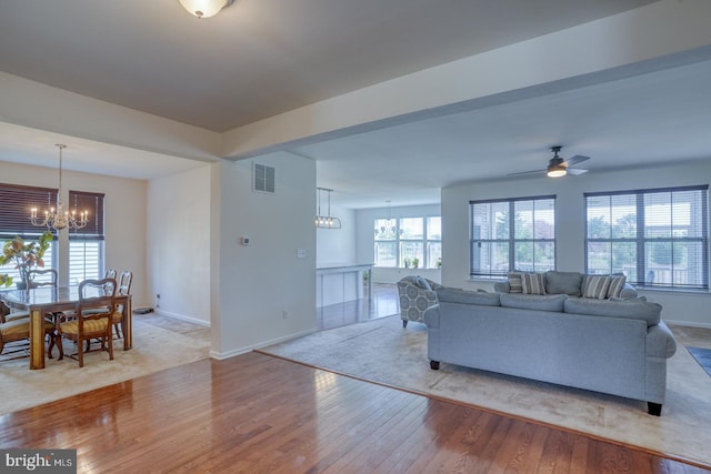 living room with visible vents, baseboards, ceiling fan with notable chandelier, and hardwood / wood-style flooring