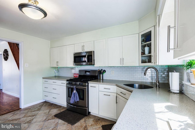 kitchen featuring decorative backsplash, glass insert cabinets, white cabinetry, a sink, and appliances with stainless steel finishes
