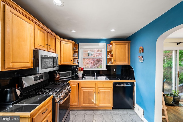 kitchen featuring open shelves, appliances with stainless steel finishes, a sink, arched walkways, and decorative backsplash