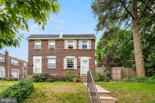view of front of house featuring brick siding, fence, a shingled roof, and a front yard