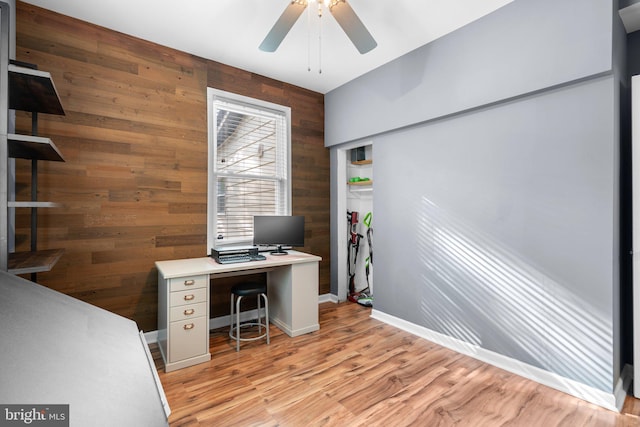 home office featuring wooden walls, light wood finished floors, an accent wall, a ceiling fan, and baseboards