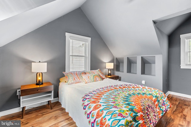 bedroom with baseboards, lofted ceiling, and wood finished floors