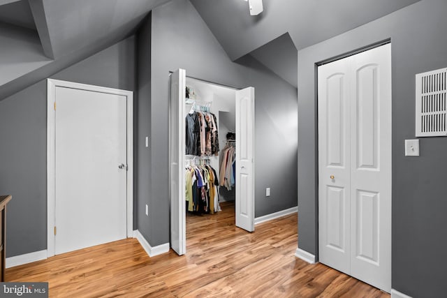 unfurnished bedroom featuring baseboards, a spacious closet, lofted ceiling, and light wood finished floors