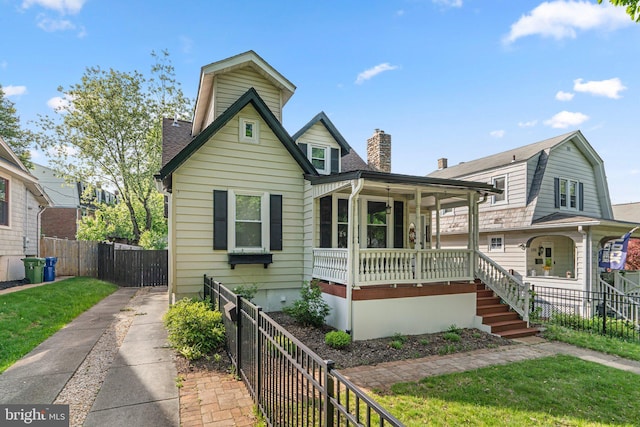 view of front of house with covered porch, a chimney, a front yard, fence, and a shingled roof