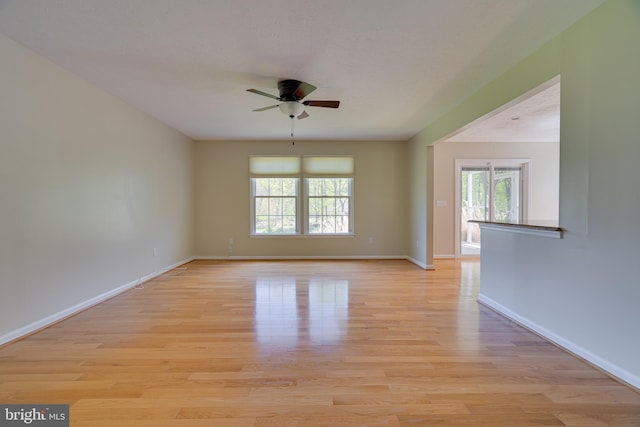 spare room featuring a healthy amount of sunlight, baseboards, a ceiling fan, and light wood-style flooring