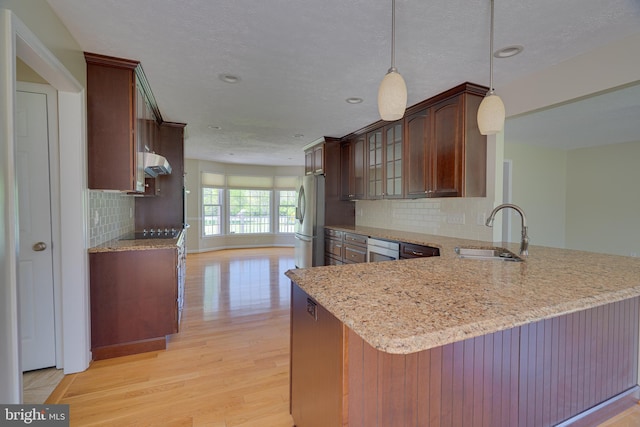 kitchen featuring tasteful backsplash, a sink, freestanding refrigerator, light wood-style floors, and under cabinet range hood