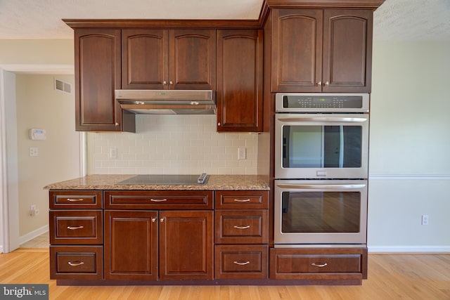 kitchen with light stone counters, double oven, black electric stovetop, and visible vents