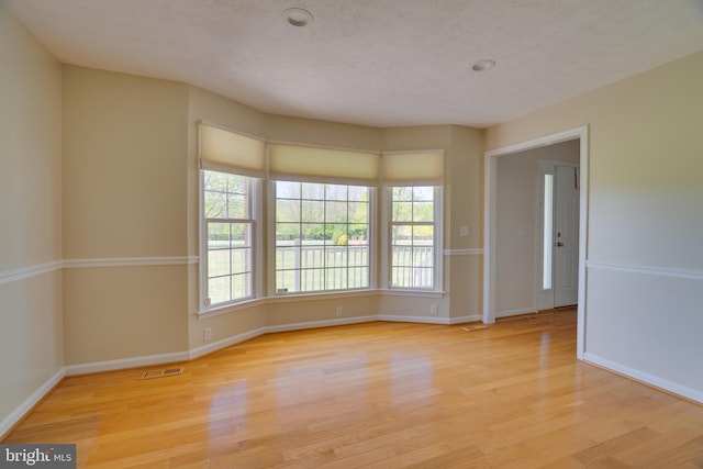 empty room featuring baseboards, a textured ceiling, light wood finished floors, and visible vents