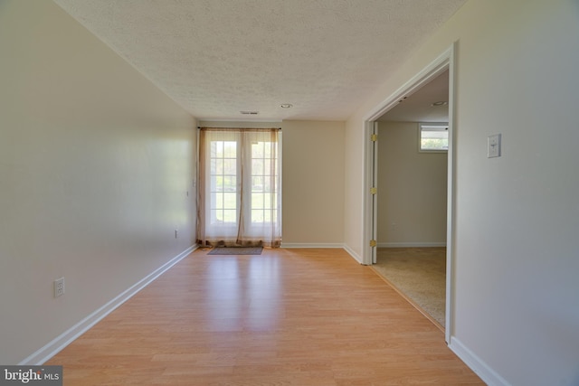 spare room featuring light wood-type flooring, a textured ceiling, baseboards, and a healthy amount of sunlight
