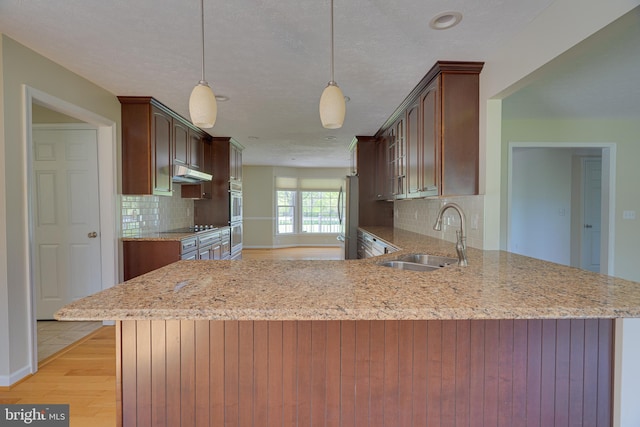 kitchen featuring a sink, freestanding refrigerator, a peninsula, backsplash, and under cabinet range hood