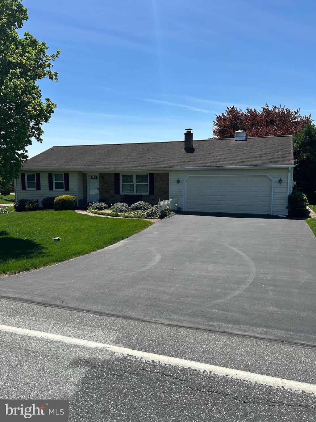 ranch-style home with an attached garage, a front lawn, aphalt driveway, and a chimney