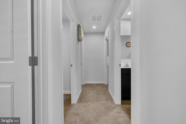 hall with light colored carpet, visible vents, a sink, baseboards, and recessed lighting