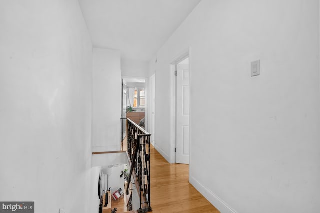 corridor with baseboards, an upstairs landing, and light wood finished floors
