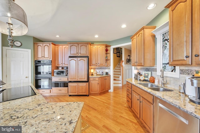 kitchen with light wood-style floors, light stone counters, a sink, backsplash, and black appliances