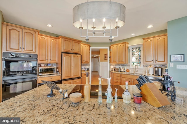 kitchen featuring dobule oven black, a sink, and light stone countertops