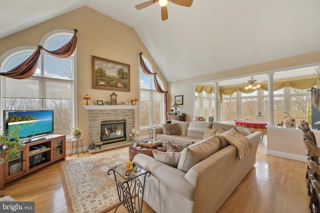 living room featuring a fireplace, high vaulted ceiling, a ceiling fan, light wood-type flooring, and ornate columns