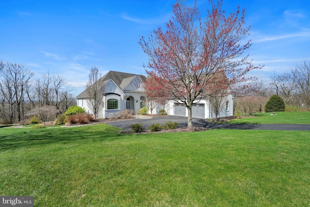 french provincial home featuring stucco siding, a garage, a front lawn, and aphalt driveway