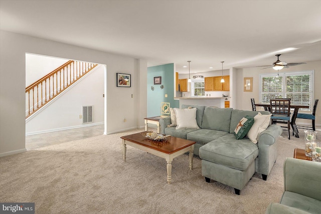 living room with ceiling fan, visible vents, baseboards, light carpet, and stairs