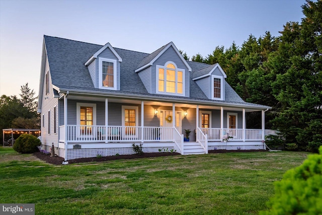 new england style home featuring a porch, a shingled roof, and a lawn
